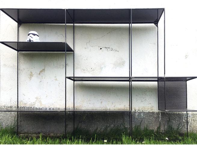 Scaffalatura metallica minimalista con casco Stormtrooper su sfondo di parete bianca.