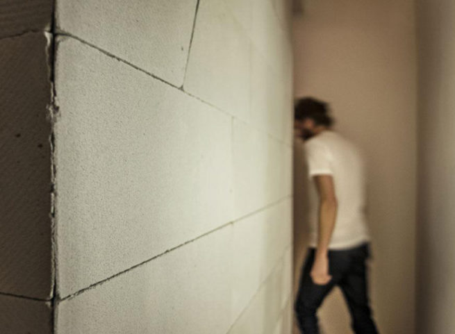 Persona sfocata che cammina in un corridoio con parete in blocchi bianchi.