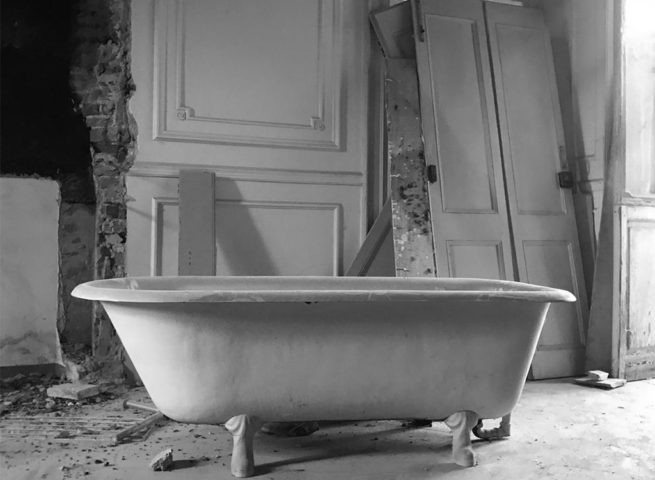 Vasca da bagno vintage in una stanza in ristrutturazione con porte e macerie sul pavimento.